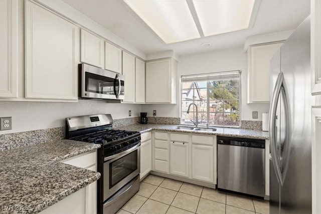 kitchen featuring sink, stone counters, white cabinetry, appliances with stainless steel finishes, and light tile patterned flooring