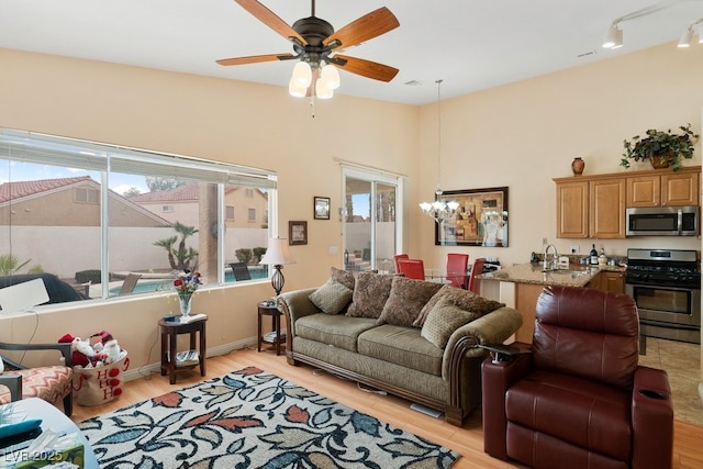 living room featuring ceiling fan with notable chandelier, light hardwood / wood-style floors, a healthy amount of sunlight, and sink