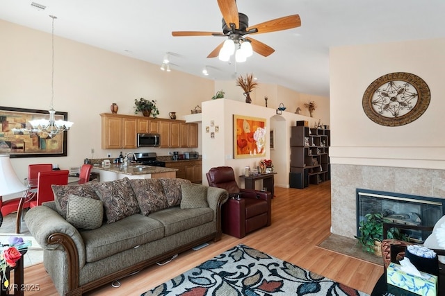 living room with sink, ceiling fan with notable chandelier, light hardwood / wood-style flooring, and a tiled fireplace