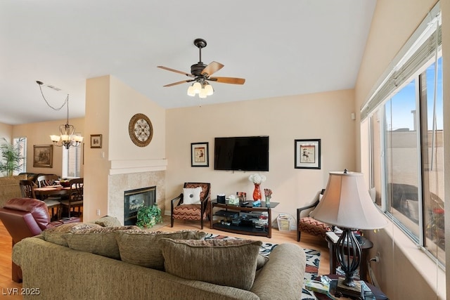 living room featuring hardwood / wood-style floors, ceiling fan with notable chandelier, and a tiled fireplace