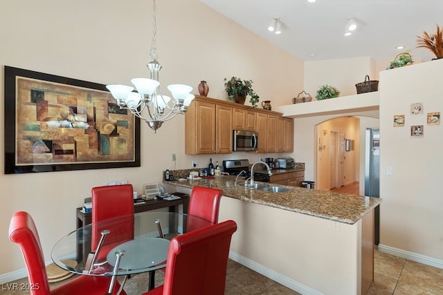 kitchen with light stone countertops, a towering ceiling, sink, an inviting chandelier, and hanging light fixtures