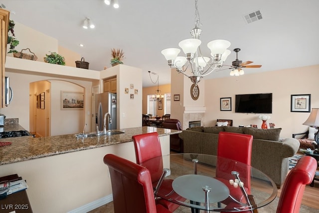 dining space with lofted ceiling, a tile fireplace, ceiling fan with notable chandelier, sink, and hardwood / wood-style flooring