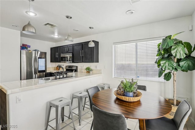 kitchen with kitchen peninsula, appliances with stainless steel finishes, sink, light tile patterned floors, and hanging light fixtures