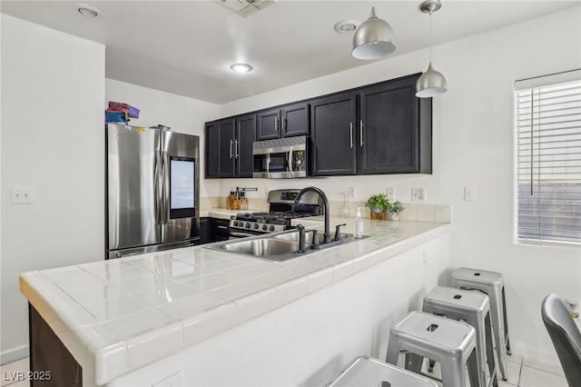 kitchen featuring pendant lighting, sink, appliances with stainless steel finishes, a kitchen bar, and kitchen peninsula