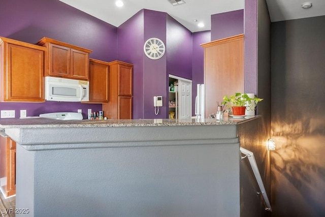 kitchen featuring kitchen peninsula, light stone counters, and a high ceiling