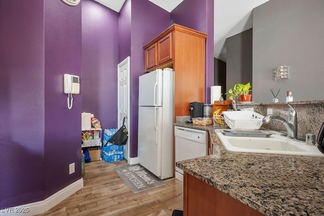 kitchen featuring light wood-type flooring, white appliances, dark stone countertops, and sink