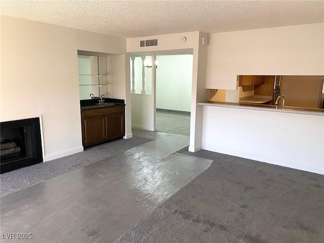 unfurnished living room featuring carpet, sink, and a textured ceiling