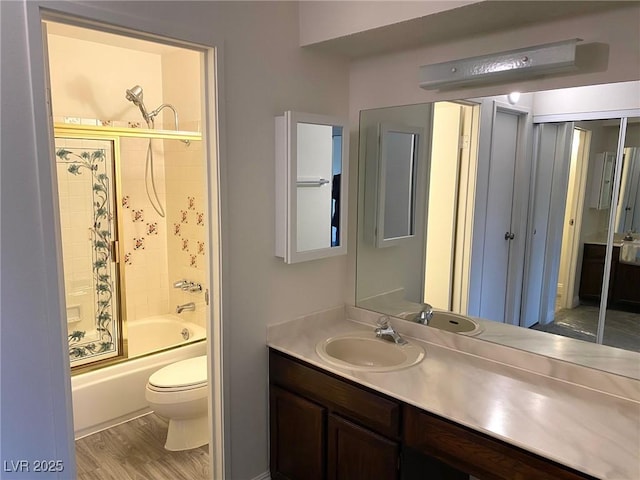 full bathroom with vanity, hardwood / wood-style flooring, toilet, and bath / shower combo with glass door