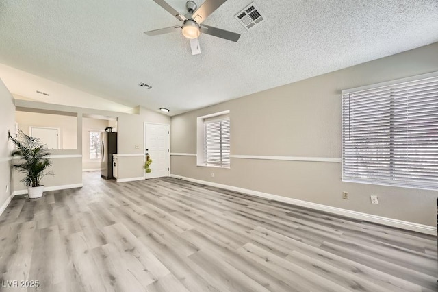 unfurnished living room featuring vaulted ceiling, a wealth of natural light, a textured ceiling, and light hardwood / wood-style flooring