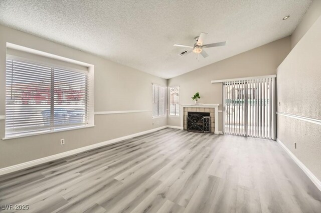 unfurnished living room featuring light hardwood / wood-style flooring, ceiling fan, a textured ceiling, a tiled fireplace, and vaulted ceiling