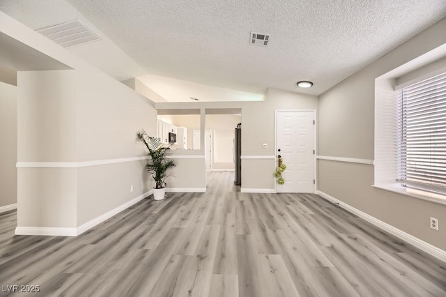 spare room featuring vaulted ceiling, light hardwood / wood-style flooring, and a textured ceiling