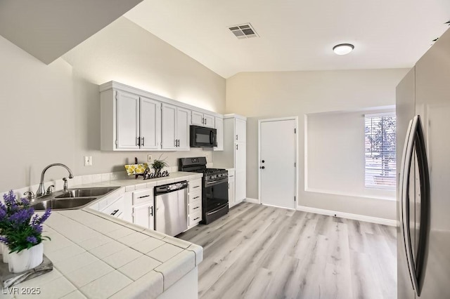 kitchen featuring sink, tile countertops, black appliances, vaulted ceiling, and white cabinets