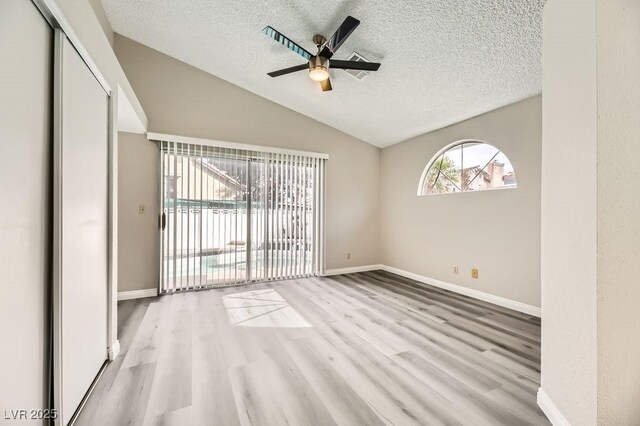 unfurnished room with ceiling fan, vaulted ceiling, a textured ceiling, and light wood-type flooring