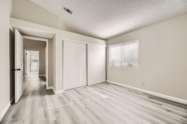 unfurnished bedroom with vaulted ceiling, a textured ceiling, a closet, and light wood-type flooring