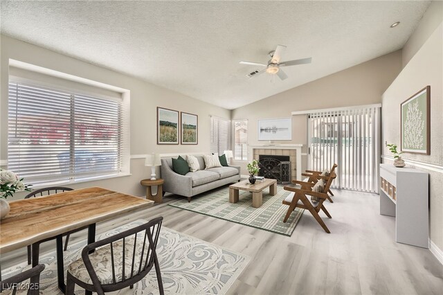 living room featuring a fireplace, lofted ceiling, ceiling fan, a textured ceiling, and light wood-type flooring