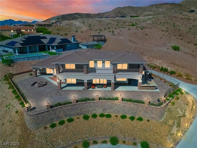 back of property at dusk featuring a patio area, a fenced backyard, a mountain view, and a balcony