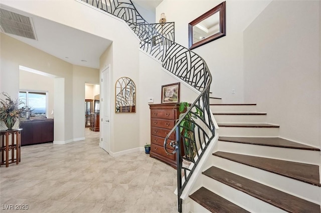 staircase featuring a high ceiling, visible vents, and baseboards