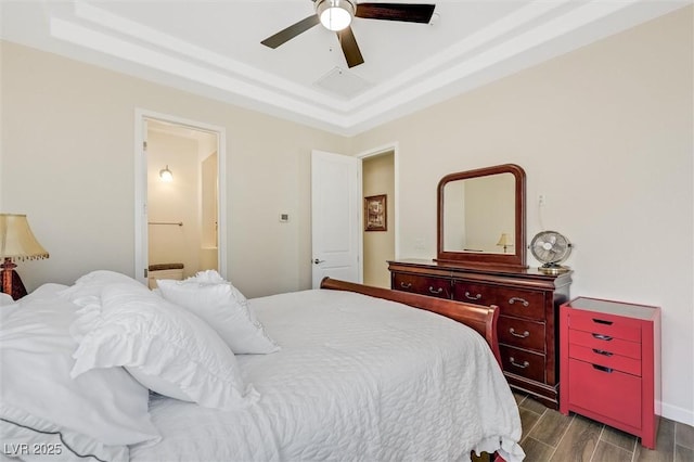 bedroom with ensuite bath, a raised ceiling, and ceiling fan