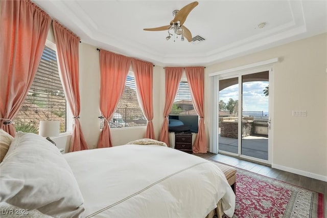 bedroom with access to exterior, a tray ceiling, wood-type flooring, and ceiling fan