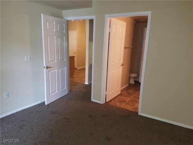 unfurnished bedroom with ensuite bath, dark carpet, and a spacious closet