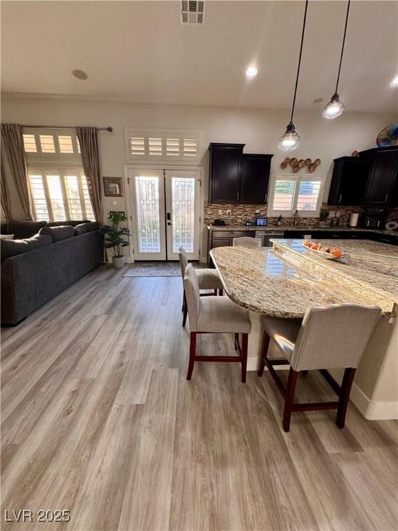 kitchen featuring decorative light fixtures, a kitchen bar, tasteful backsplash, light hardwood / wood-style floors, and light stone counters