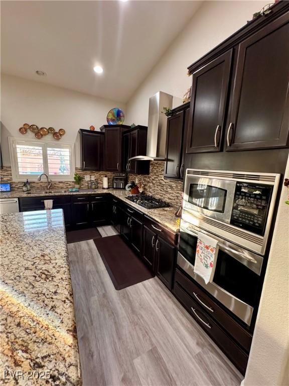 kitchen with light stone counters, backsplash, wall chimney range hood, and stainless steel appliances