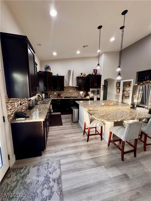 kitchen with sink, decorative light fixtures, backsplash, light stone counters, and wall chimney exhaust hood