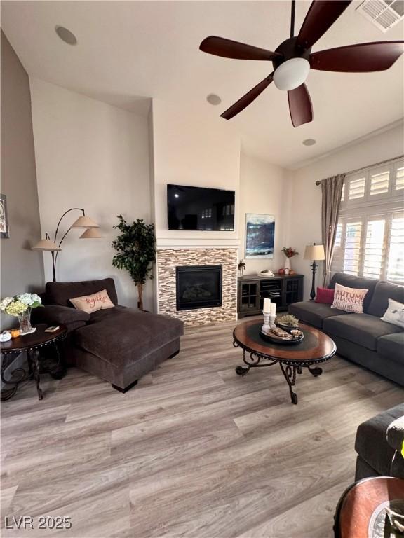 living room featuring light wood-type flooring, ceiling fan, and a fireplace