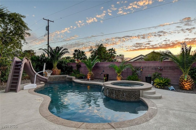 pool at dusk featuring an in ground hot tub and a water slide