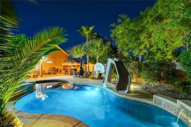 pool at night with a patio and a water slide