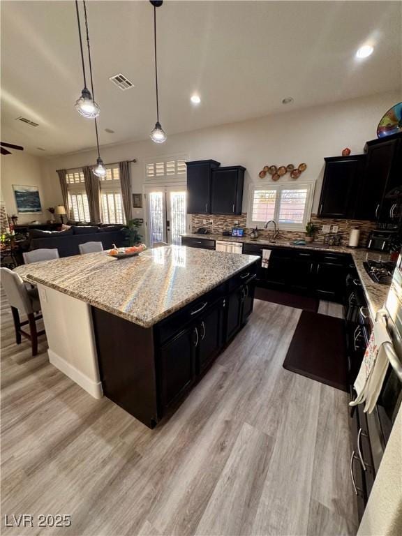 kitchen featuring ceiling fan, decorative light fixtures, light wood-type flooring, tasteful backsplash, and a kitchen island