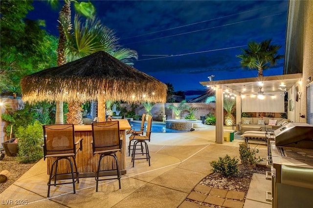 patio at night featuring a bar, a fenced in pool, and outdoor lounge area