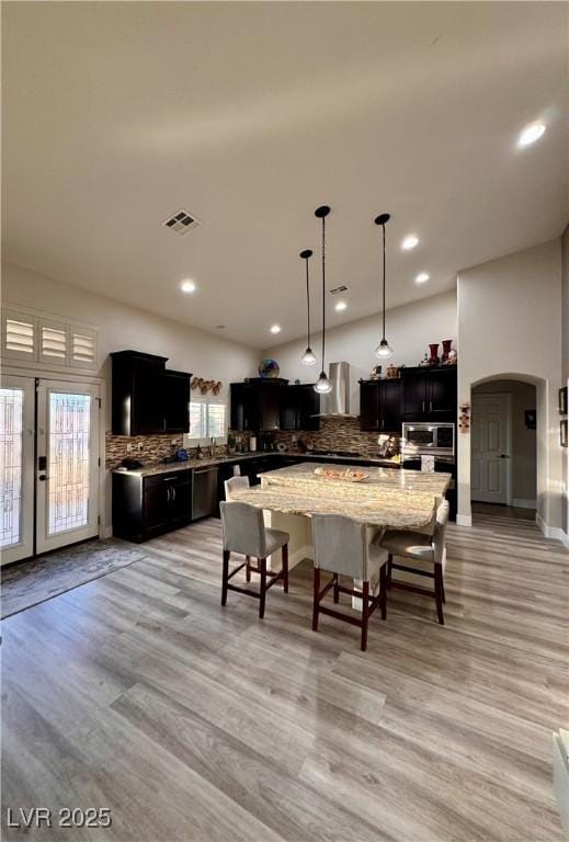 kitchen with light hardwood / wood-style flooring, hanging light fixtures, light stone counters, a center island, and decorative backsplash