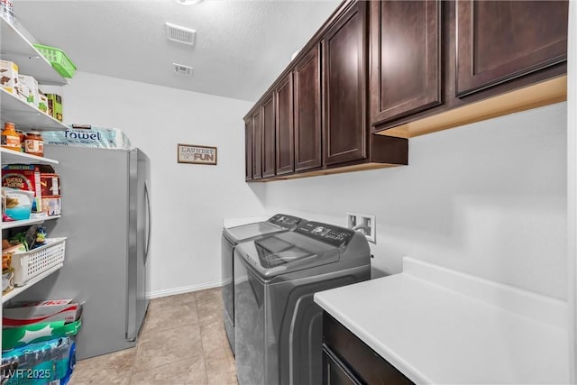 clothes washing area featuring a textured ceiling, light tile patterned floors, cabinets, and independent washer and dryer