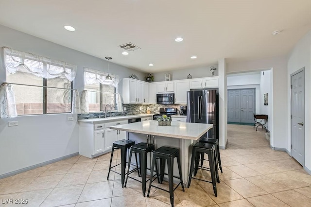 kitchen with a center island, black range with gas stovetop, hanging light fixtures, stainless steel fridge, and white cabinetry