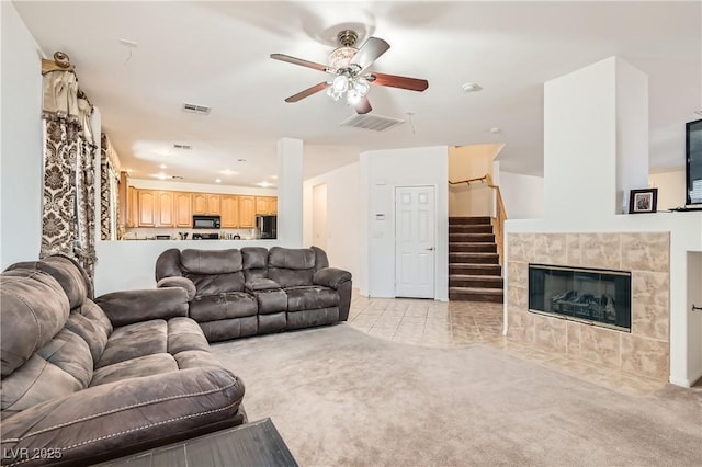 living room featuring a ceiling fan, a tile fireplace, visible vents, and light colored carpet