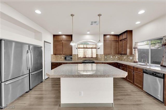 kitchen with pendant lighting, sink, appliances with stainless steel finishes, a kitchen island, and decorative backsplash