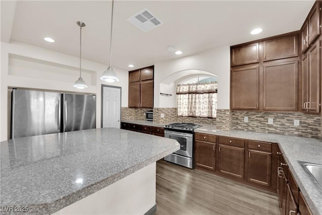 kitchen with tasteful backsplash, hanging light fixtures, appliances with stainless steel finishes, light stone countertops, and hardwood / wood-style floors