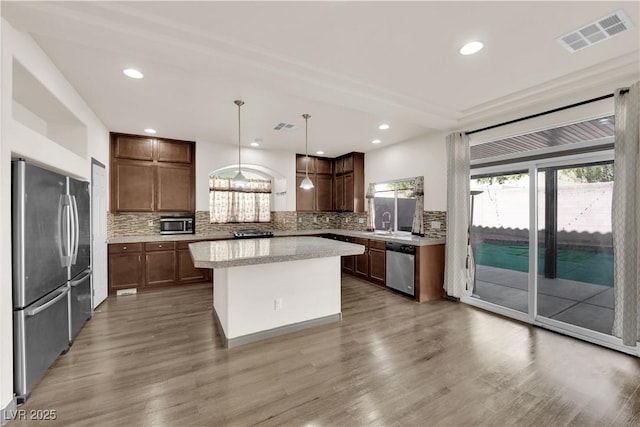 kitchen featuring a kitchen island, appliances with stainless steel finishes, decorative backsplash, and decorative light fixtures