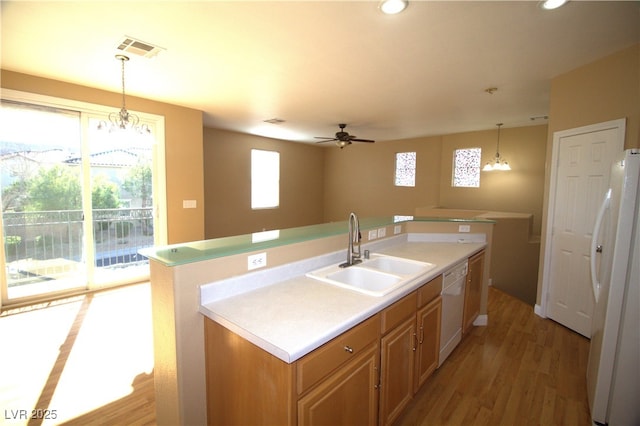 kitchen featuring ceiling fan with notable chandelier, white appliances, decorative light fixtures, an island with sink, and sink