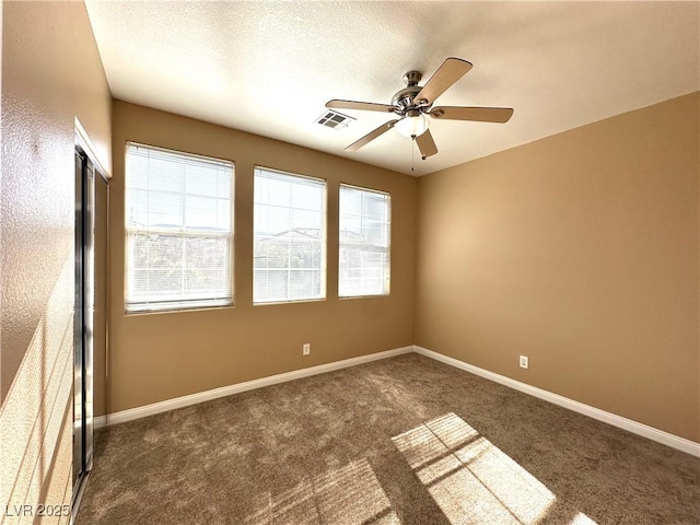 empty room with ceiling fan and dark colored carpet