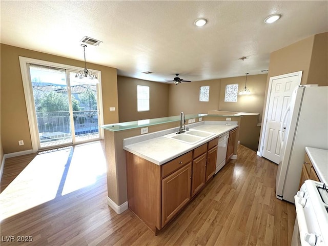 kitchen with pendant lighting, sink, white appliances, ceiling fan with notable chandelier, and an island with sink