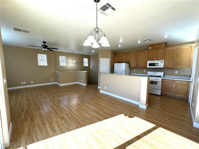 kitchen with ceiling fan with notable chandelier, white appliances, a center island, hanging light fixtures, and dark hardwood / wood-style floors