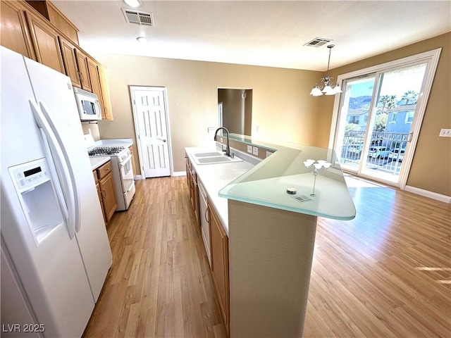 kitchen with white appliances, a chandelier, a kitchen island with sink, sink, and decorative light fixtures