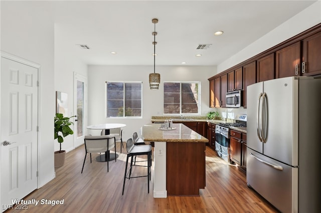 kitchen featuring a kitchen breakfast bar, light stone counters, pendant lighting, a kitchen island, and appliances with stainless steel finishes