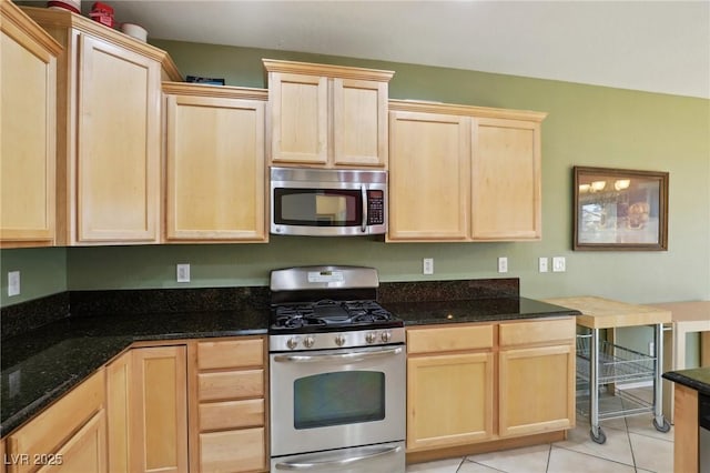 kitchen featuring dark stone countertops, light brown cabinetry, light tile patterned flooring, and appliances with stainless steel finishes