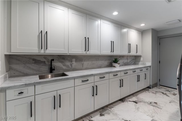 kitchen featuring recessed lighting, marble finish floor, a sink, white cabinetry, and tasteful backsplash