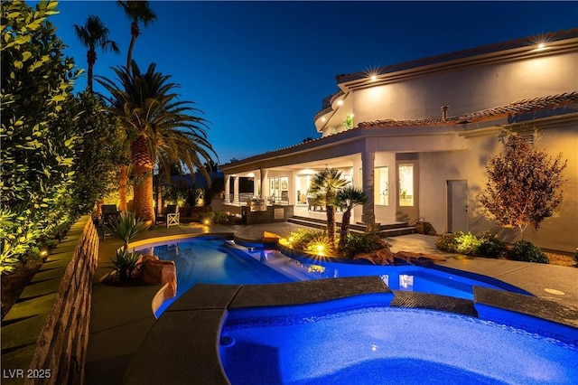 pool at night featuring an outdoor pool, a patio, and an in ground hot tub