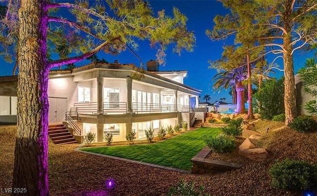 back of house with stairway, a lawn, and stucco siding