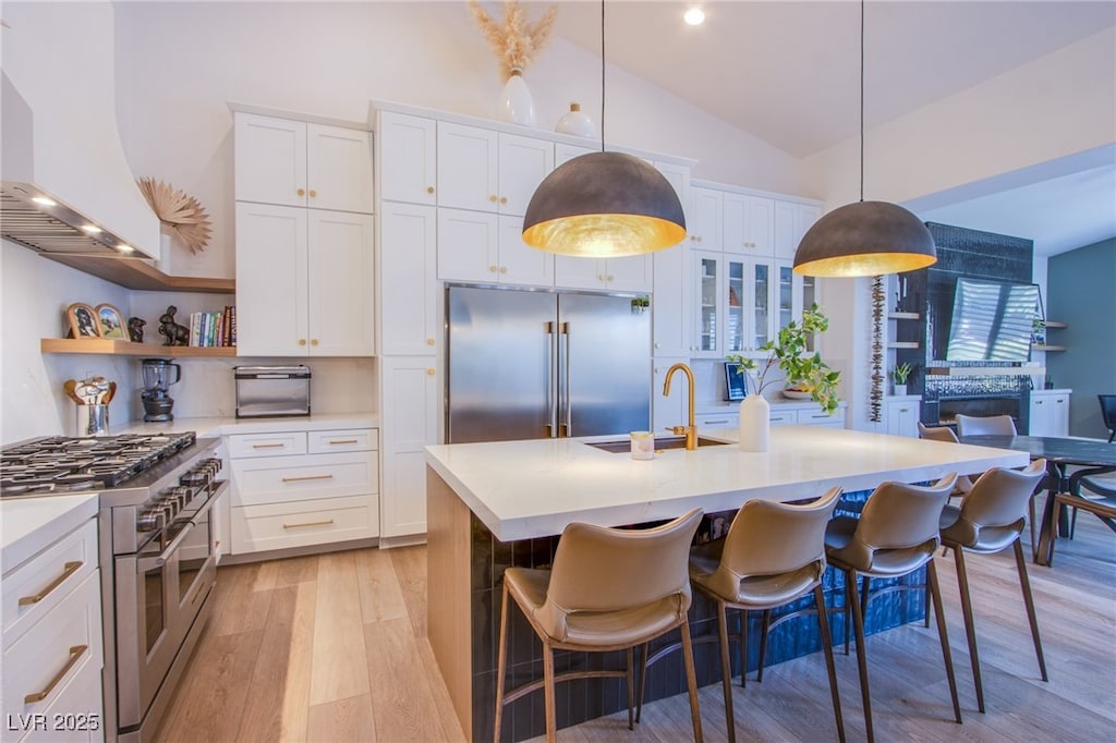 kitchen with sink, wall chimney range hood, vaulted ceiling, white cabinets, and high end appliances